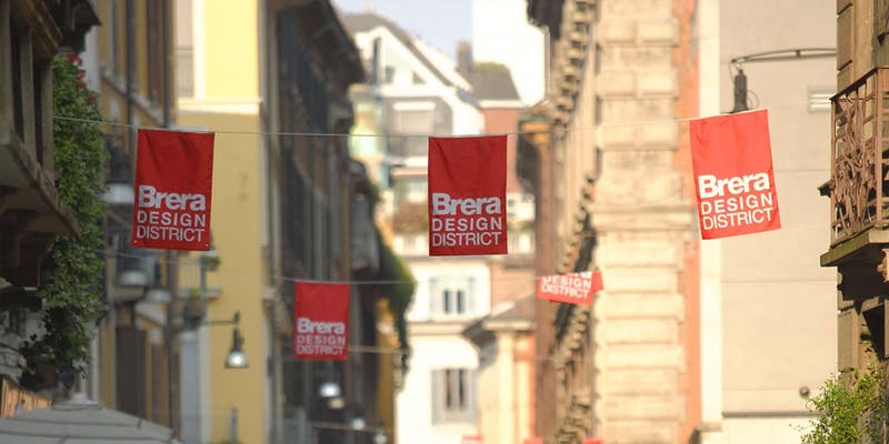 street scene in milan with red flags with white text of brera design district